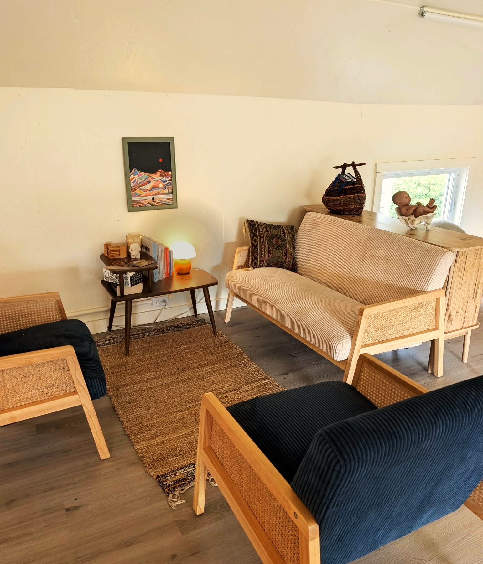Le salon à l'étage de la grange : causeuse en velours côtelé, fauteuils en cannage et tapis de jute